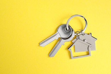 Photo of Keys with keychain in shape of house on yellow background, top view. Space for text