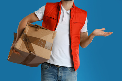Photo of Courier with damaged cardboard box on blue background, closeup. Poor quality delivery service