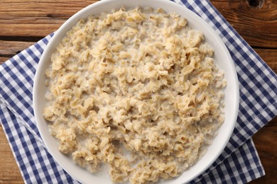 Photo of Tasty boiled oatmeal in bowl on wooden table, top view