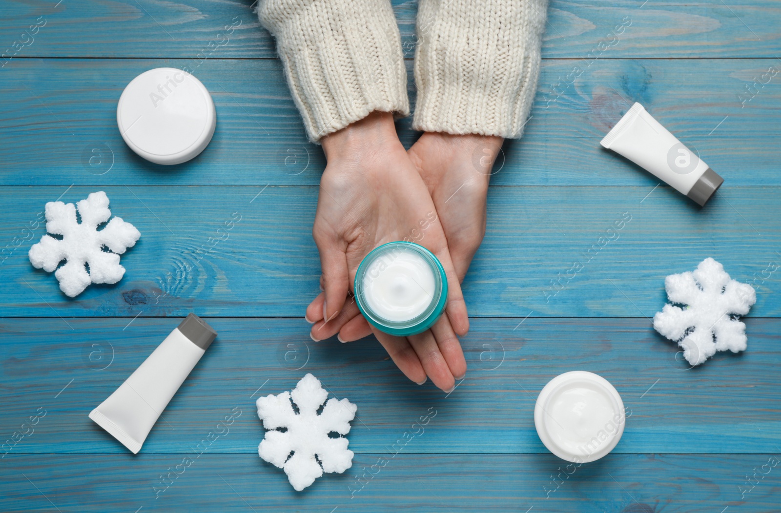 Photo of Woman with jar of hand cream at turquoise wooden table, top view