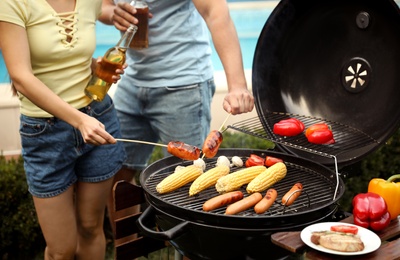 People with beer and sausages near barbecue grill outdoors, closeup