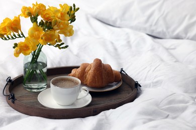 Photo of Morning coffee, croissant and flowers on bed, space for text