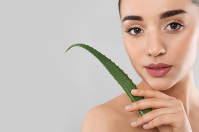 Photo of Young woman with aloe vera leaf on light grey background, closeup. Space for text