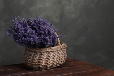 Beautiful fresh lavender flowers in wicker basket on wooden table against grey background. Space for text