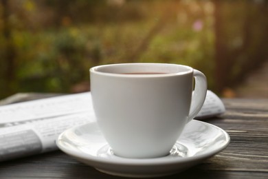 Photo of White cup with coffee and newspaper on wooden table, closeup. Morning ritual