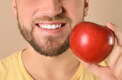 Young man with healthy teeth and apple on color background, closeup