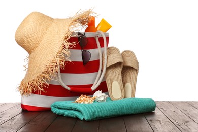 Stylish bag with beach accessories on wooden table against white background