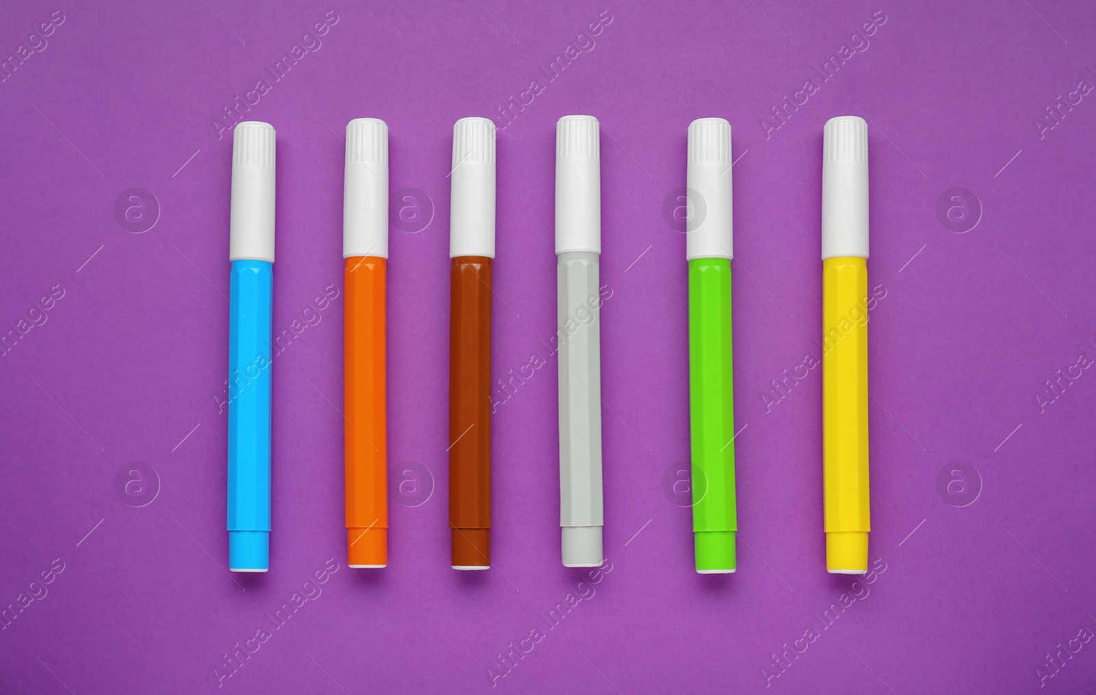 Photo of Different colorful markers on purple background, flat lay