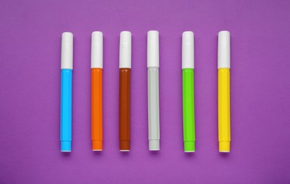 Photo of Different colorful markers on purple background, flat lay