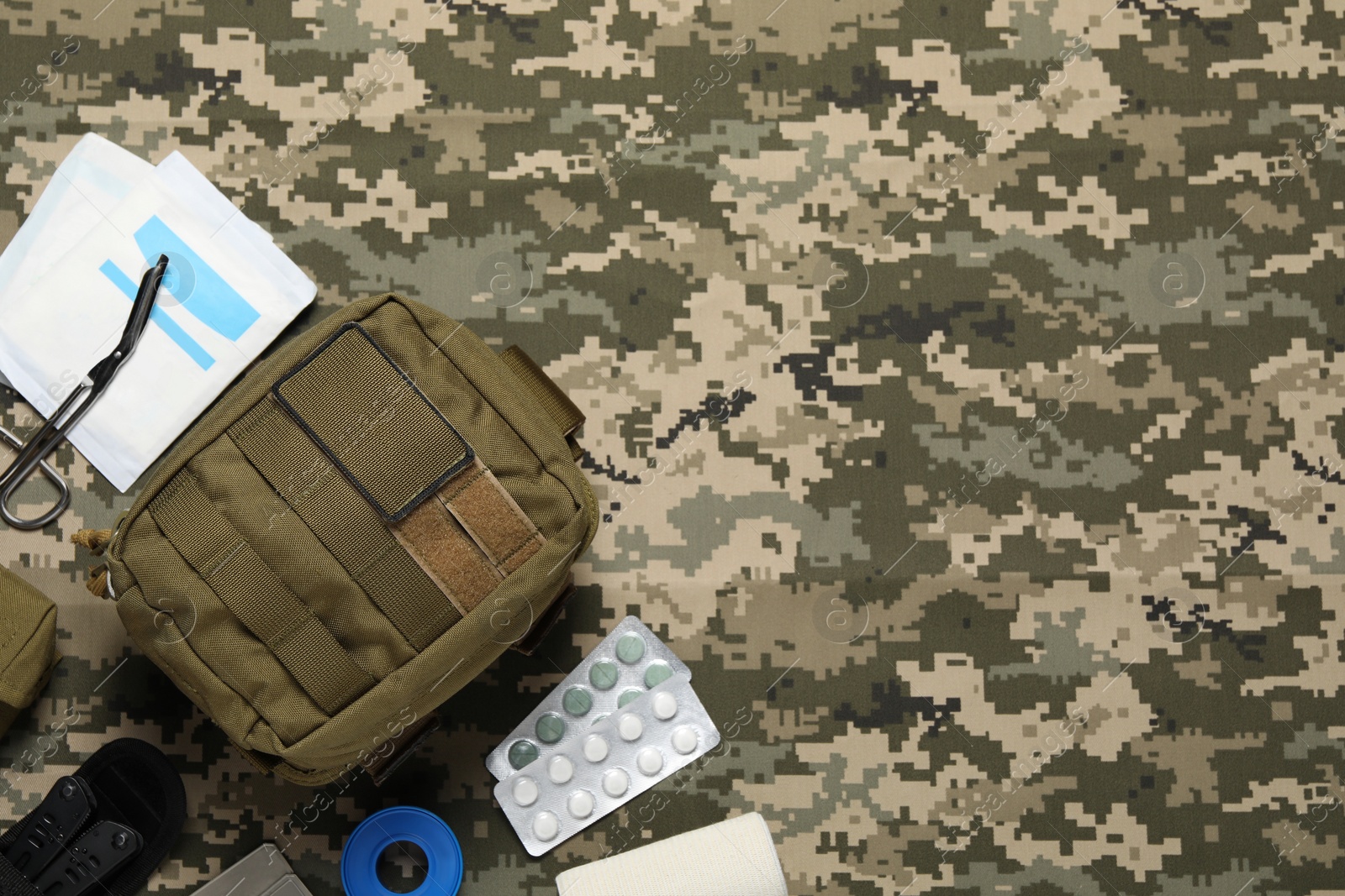 Photo of Flat lay composition with military first aid kit on camouflage fabric. Space for text