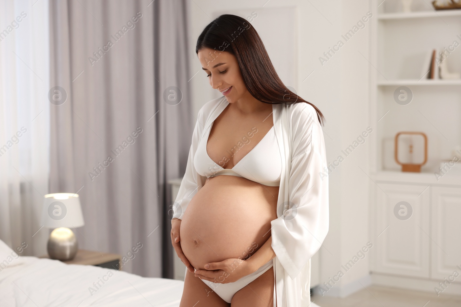 Photo of Beautiful pregnant woman wearing stylish comfortable underwear and robe in bedroom