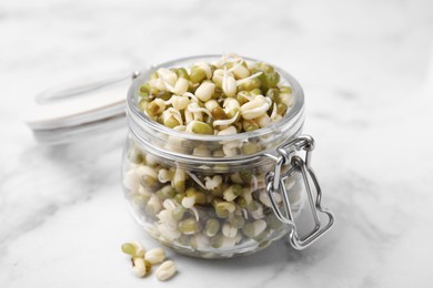 Glass jar with sprouted green mung beans on white marble table, closeup