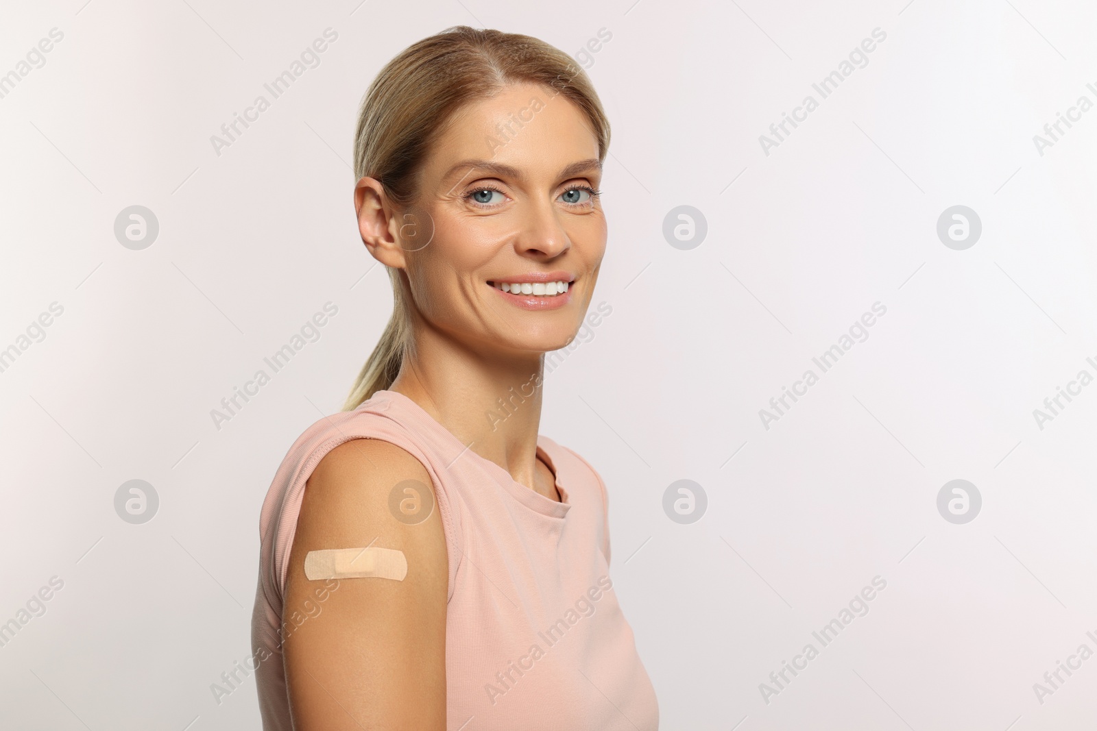 Photo of Smiling woman with adhesive bandage on arm after vaccination on light background. Space for text