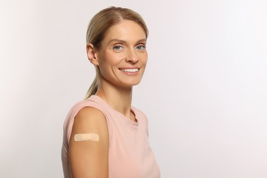 Photo of Smiling woman with adhesive bandage on arm after vaccination on light background. Space for text