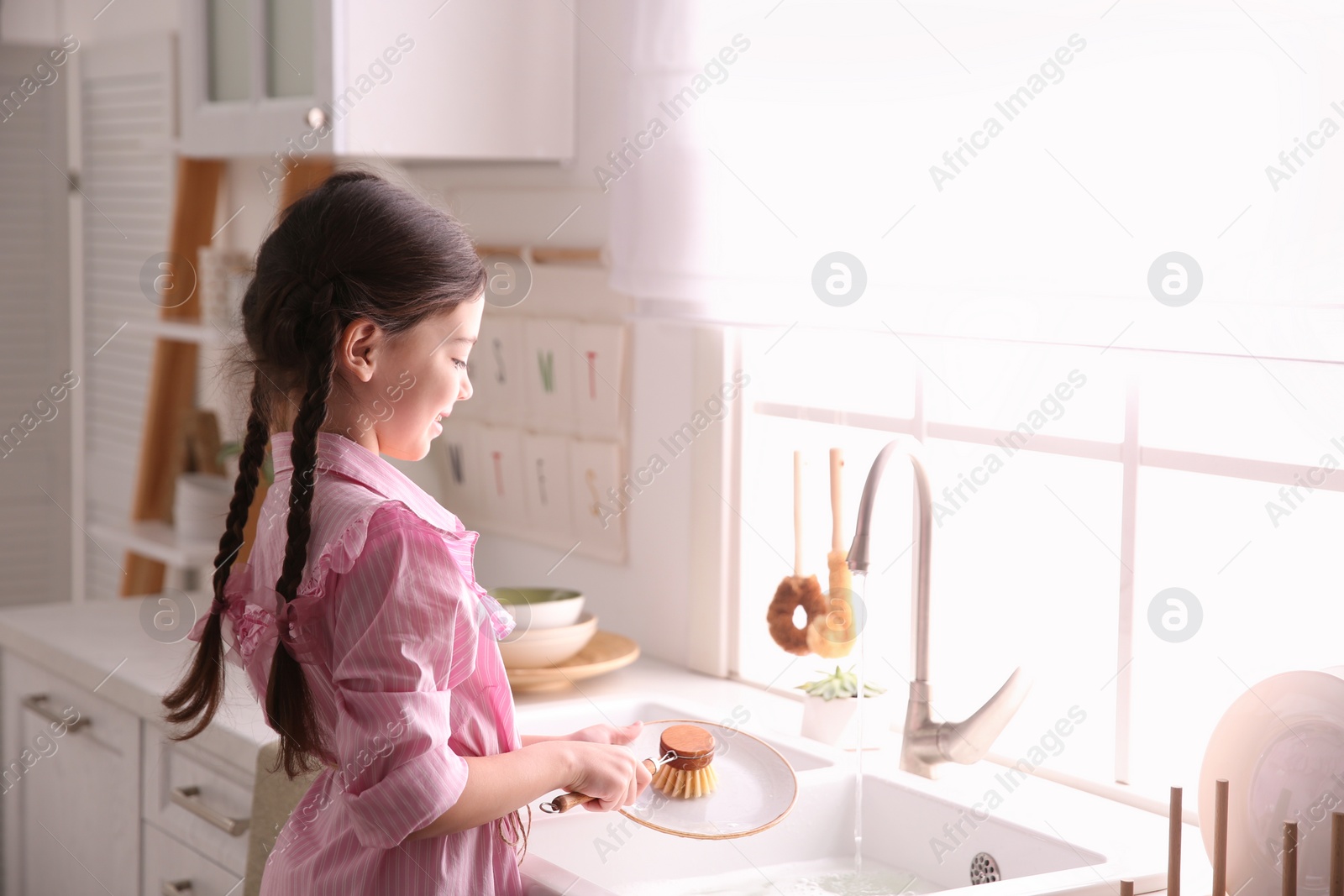 Photo of Little girl washing dishes in kitchen at home