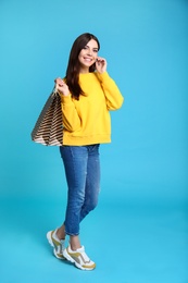 Full length portrait of young woman with paper bags on blue background