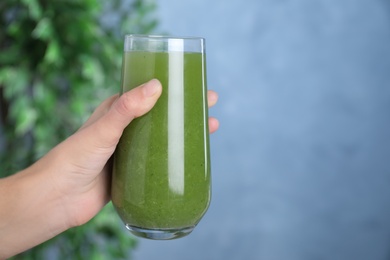 Photo of Woman holding glass of fresh celery juice against blurred background, closeup. Space for text