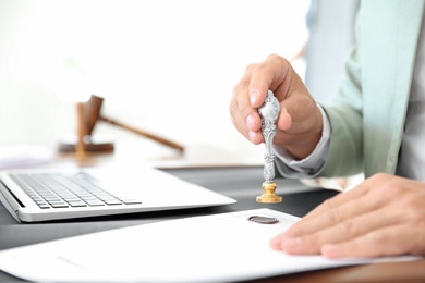 Photo of Male notary stamping document at table in office, closeup