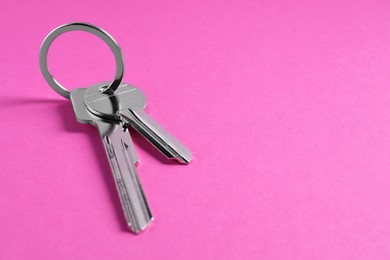 Keys with ring on pink background, closeup. Space for text