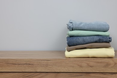 Photo of Stack of different folded clothes on wooden table near grey wall, space for text