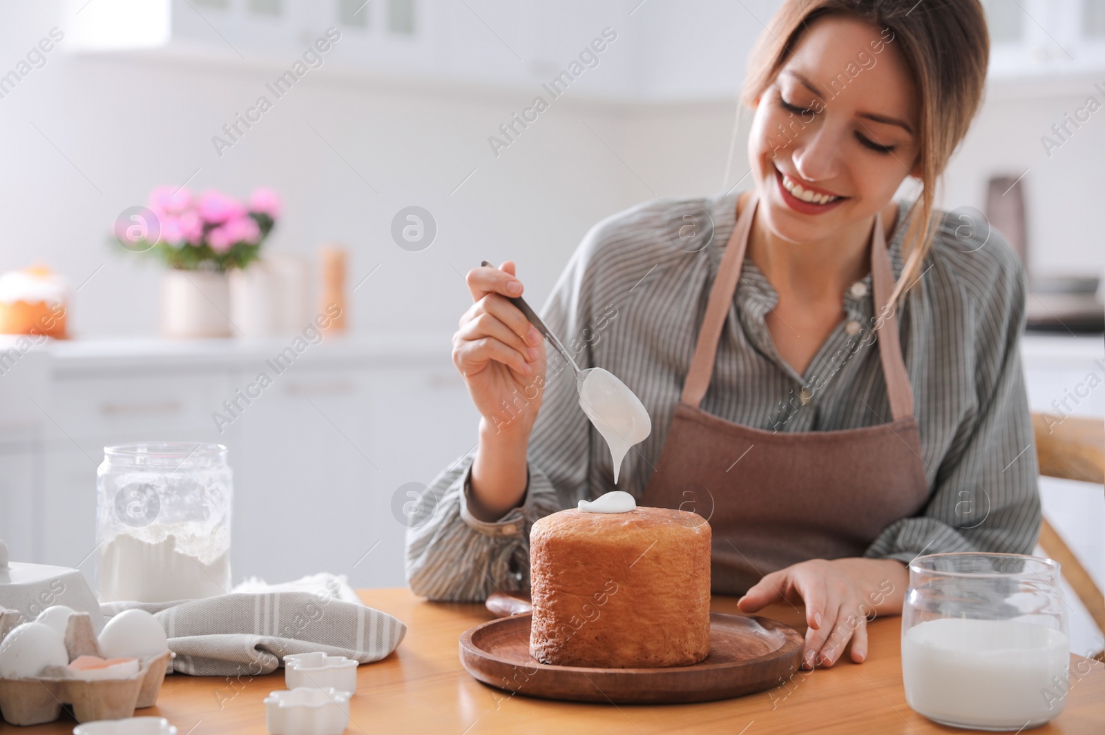 Photo of Young woman decorating traditional Easter cake with glaze in kitchen. Space for text