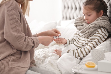 Mother giving pills to little daughter suffering from cold in bed