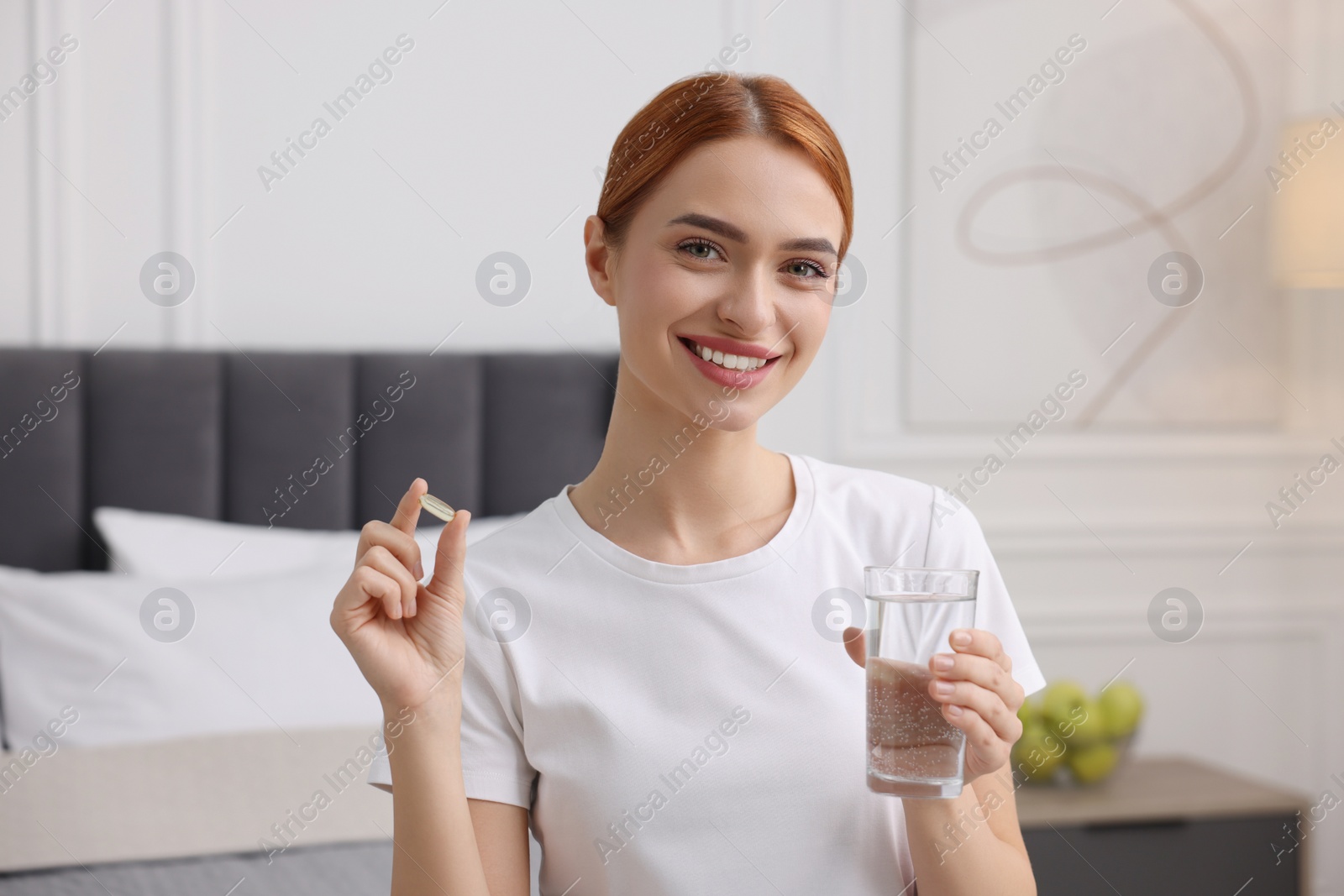 Photo of Happy young woman with pill and glass of water in room. Weight loss