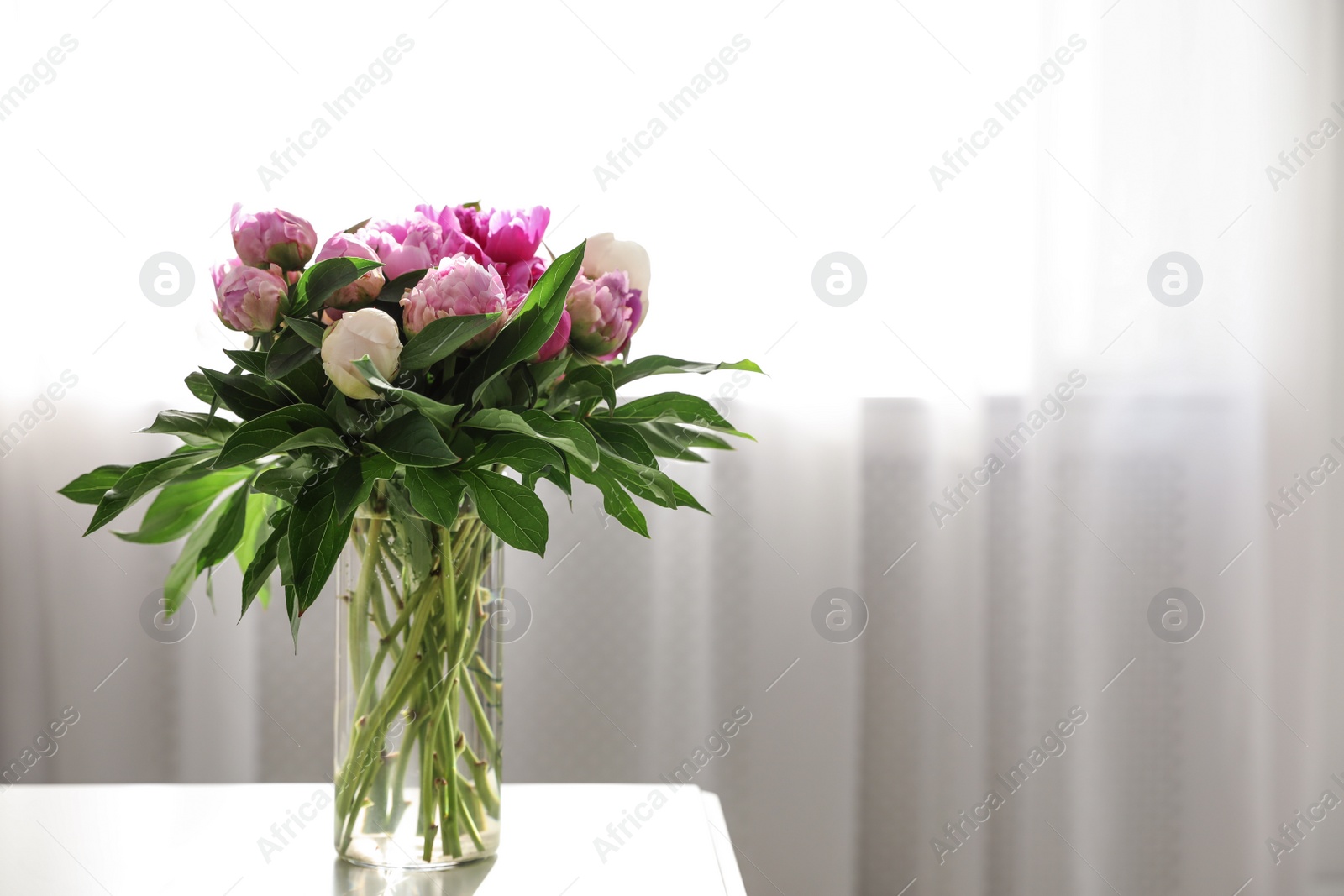 Photo of Vase with bouquet of beautiful peonies on table in room, space for text