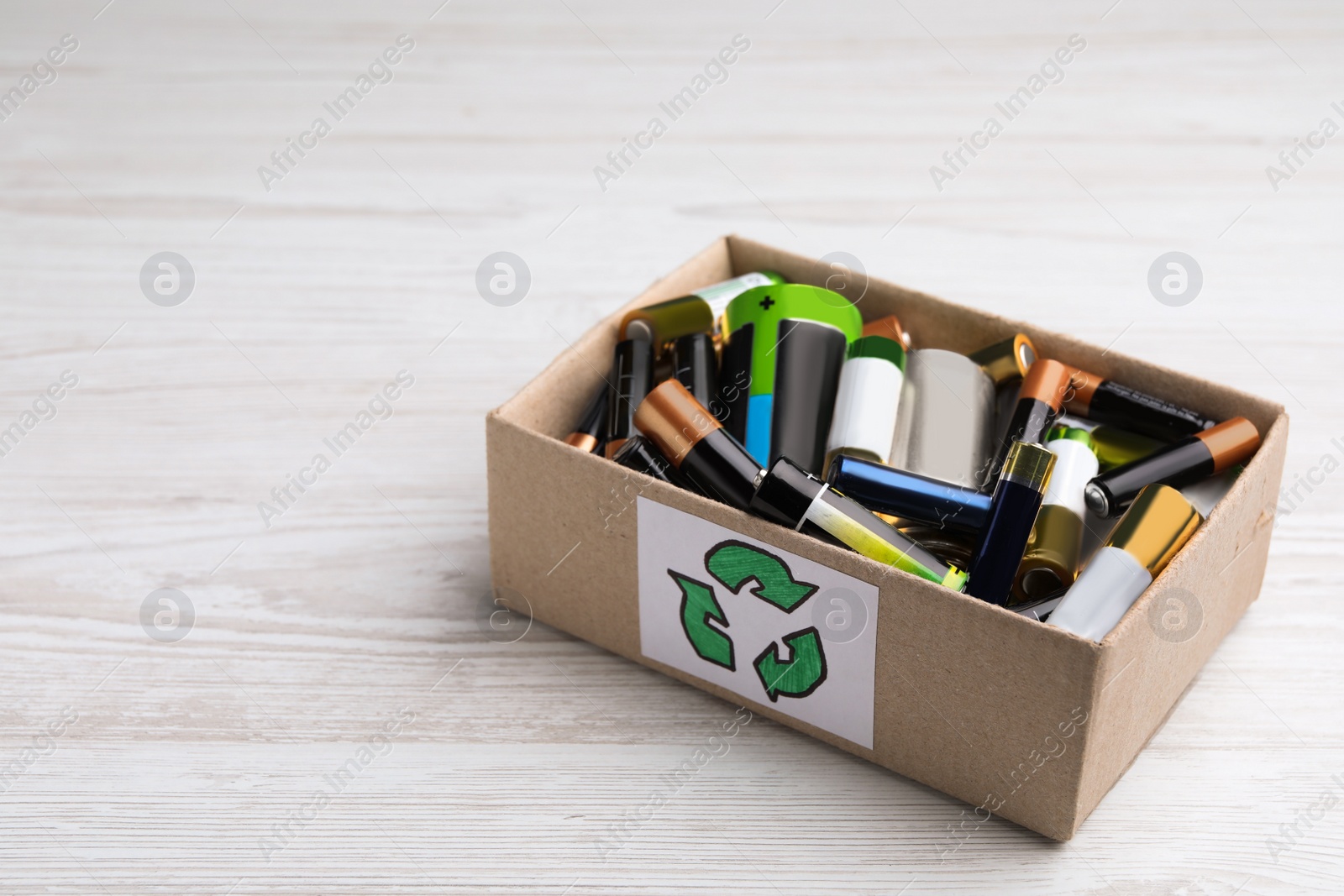 Image of Used batteries in cardboard box with recycling symbol on white wooden table, space for text