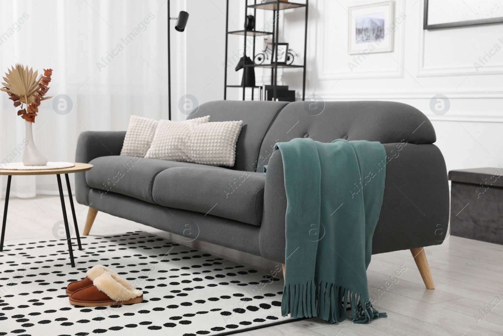 Photo of Stylish living room interior with comfortable sofa, blanket, slippers and side table