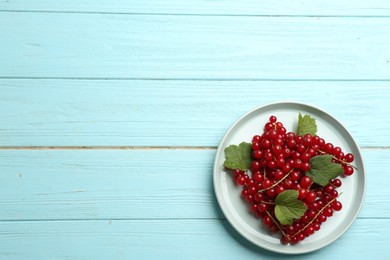 Photo of Delicious red currants and leaves on light blue wooden table, top view. Space for text