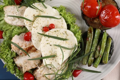 Photo of Tasty mozzarella, chicken and vegetables with tarragon on white plate, top view