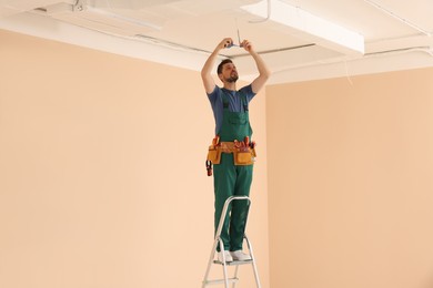 Photo of Electrician in uniform with insulating tape repairing ceiling wiring indoors. Space for text