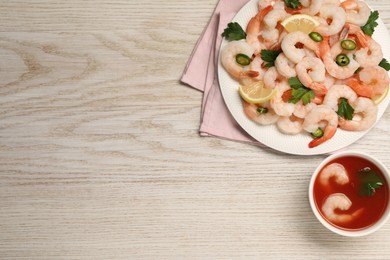 Photo of Tasty boiled shrimps with cocktail sauce, chili, parsley and lemon on light wooden table, flat lay. Space for text