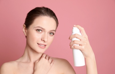 Young woman with bottle of thermal water on color background. Cosmetic product