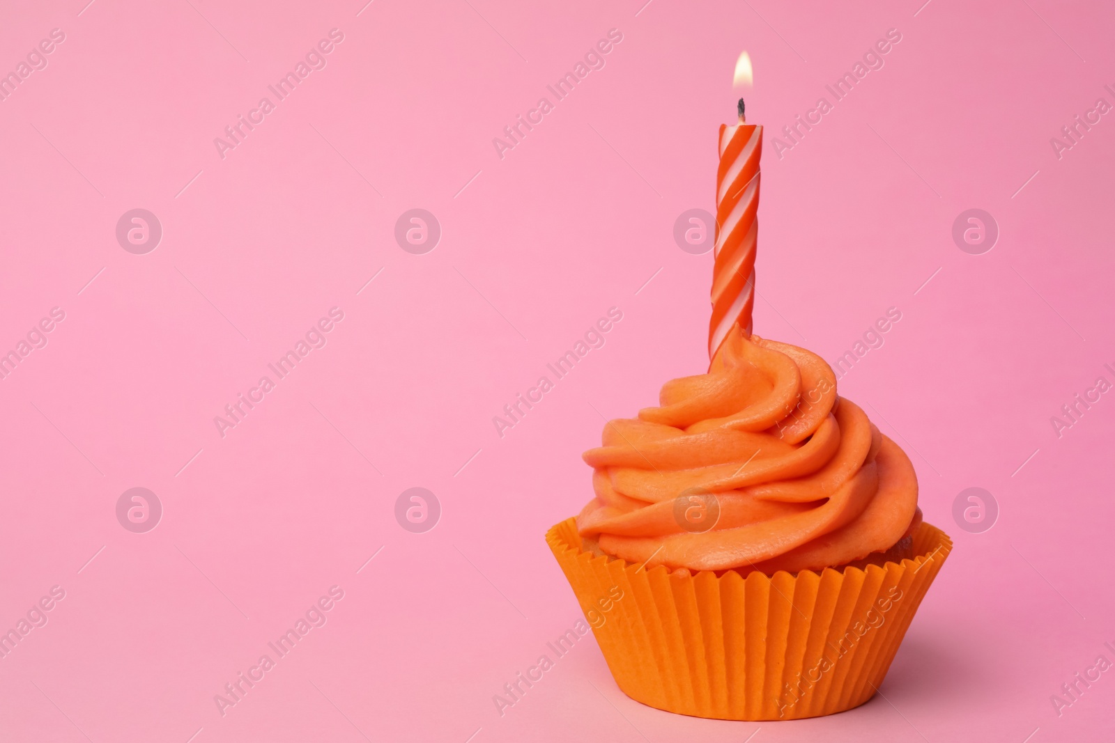 Photo of Delicious birthday cupcake with orange cream and burning candle on pink background. Space for text