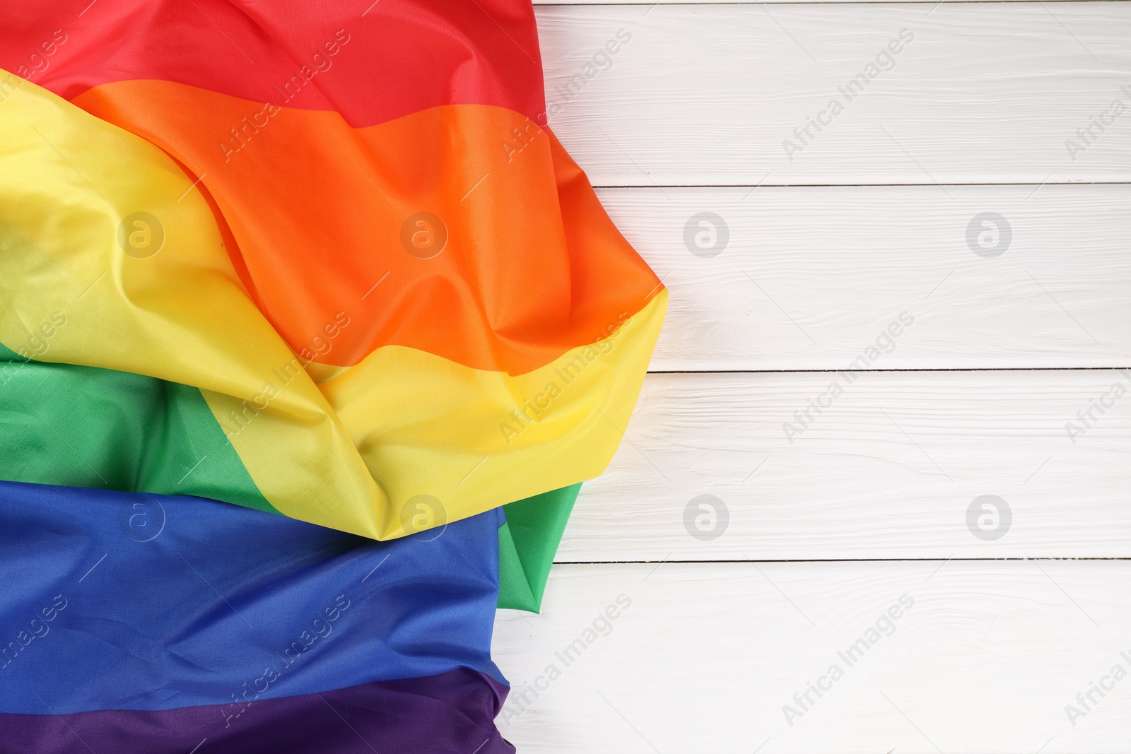 Photo of Rainbow LGBT flag on white wooden table, top view. Space for text