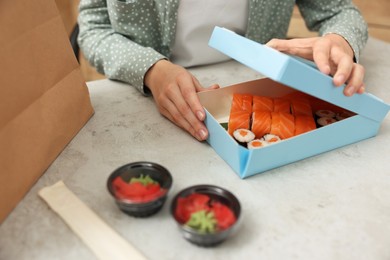 Photo of Woman unpacking her order from sushi restaurant at table in kitchen, closeup
