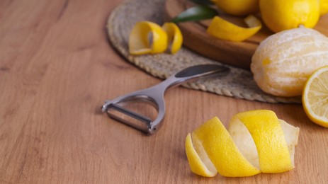 Photo of Lemon zest. Rind, fresh fruits and peeler on wooden table, space for text