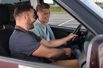 Photo of Driving school. Happy student during lesson with driving instructor in car at parking lot
