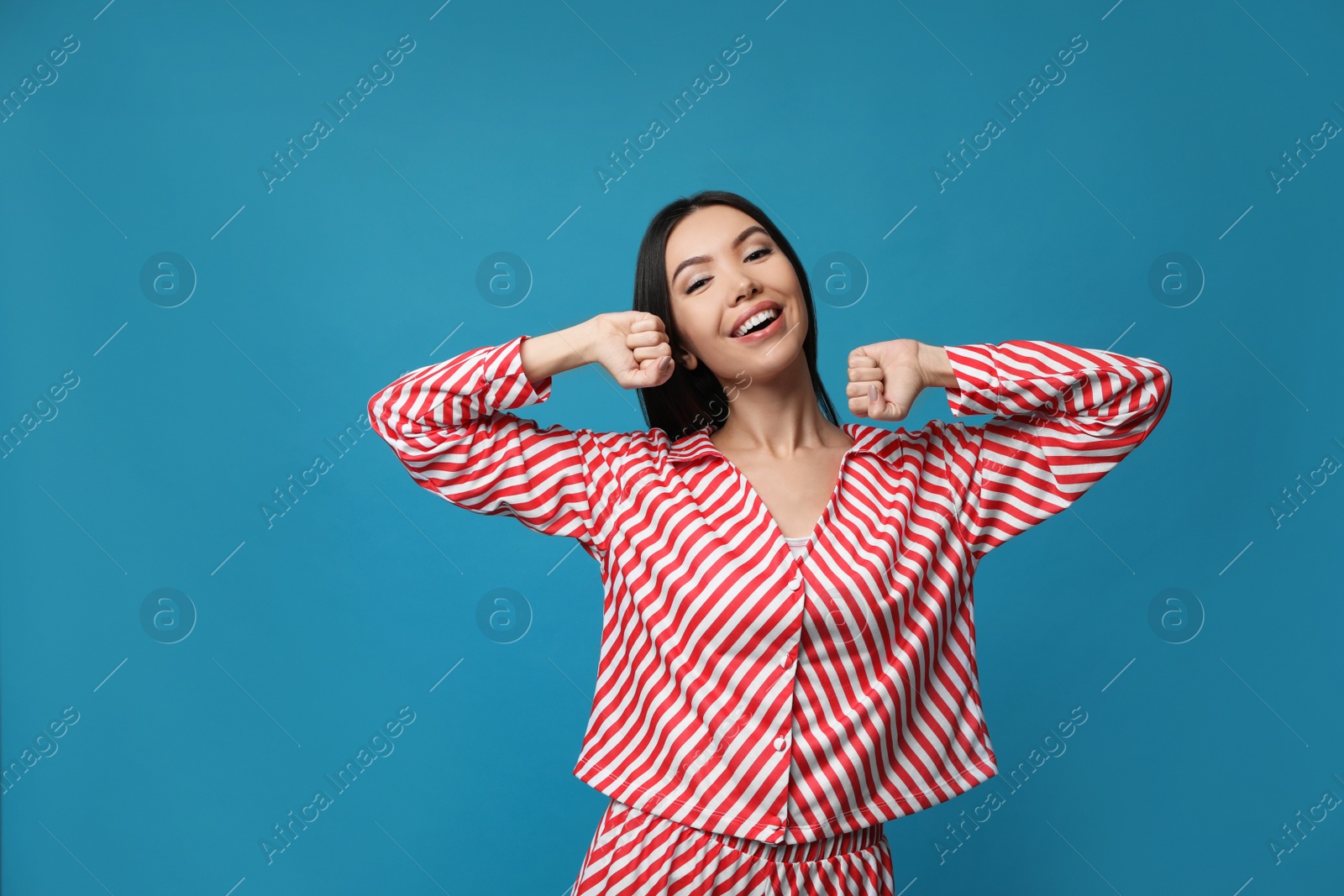 Photo of Beautiful Asian woman in pajamas stretching on blue background. Bedtime