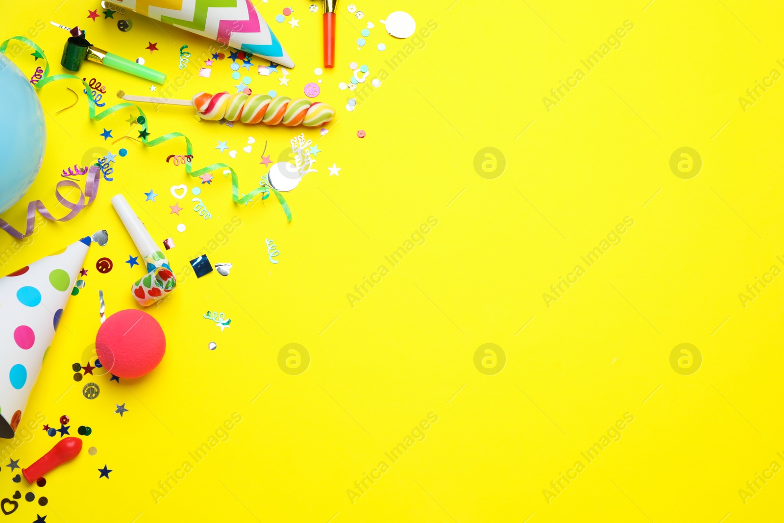 Photo of Flat lay composition with party hats and other festive items on yellow background, space for text. Birthday surprise