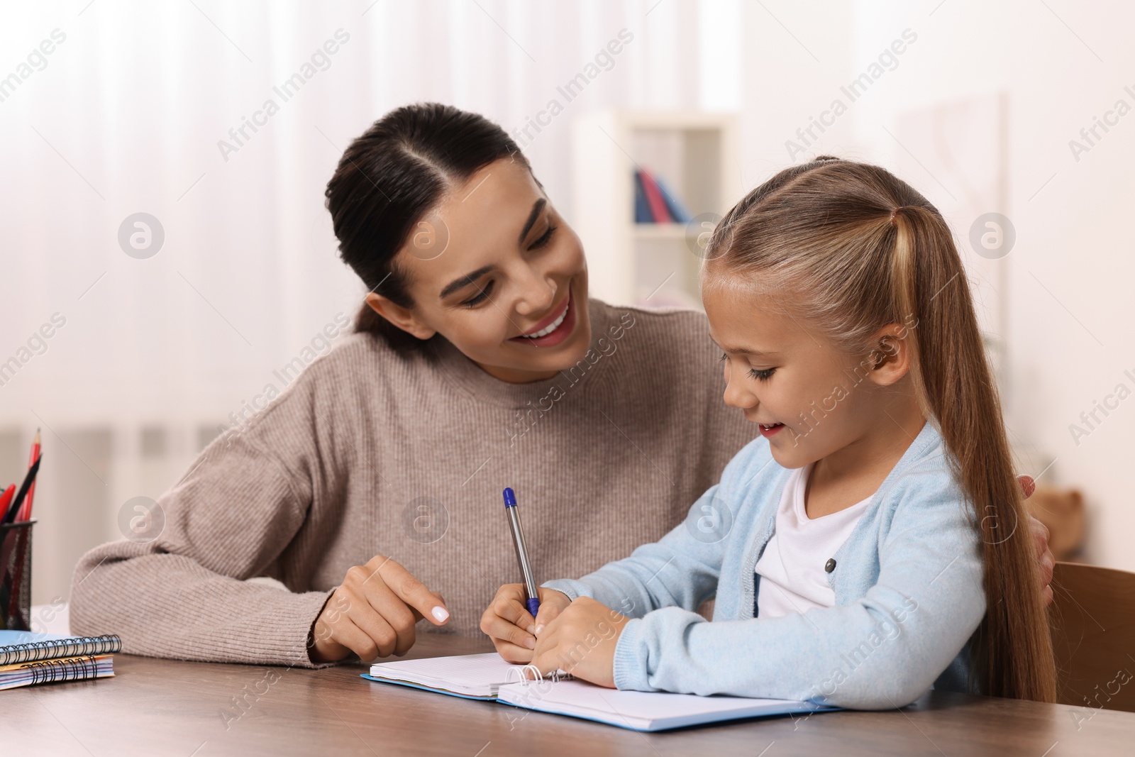 Photo of Dyslexia problem. Mother helping daughter with homework at table in room