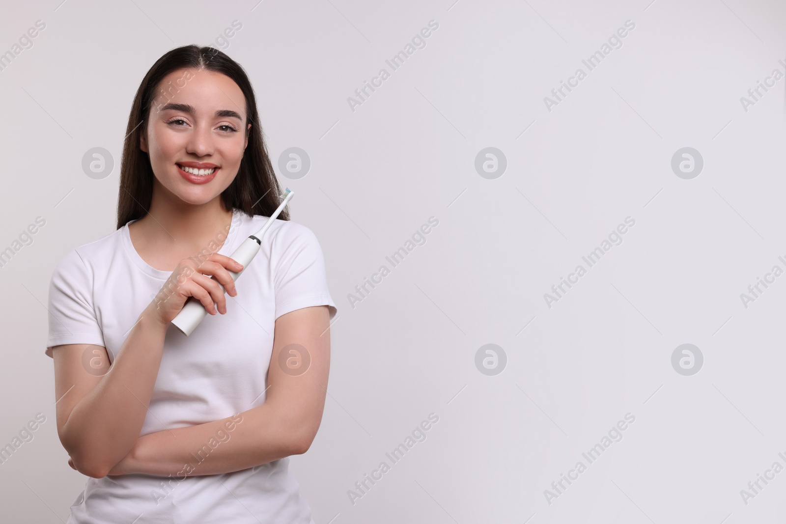 Photo of Happy young woman holding electric toothbrush on white background, space for text