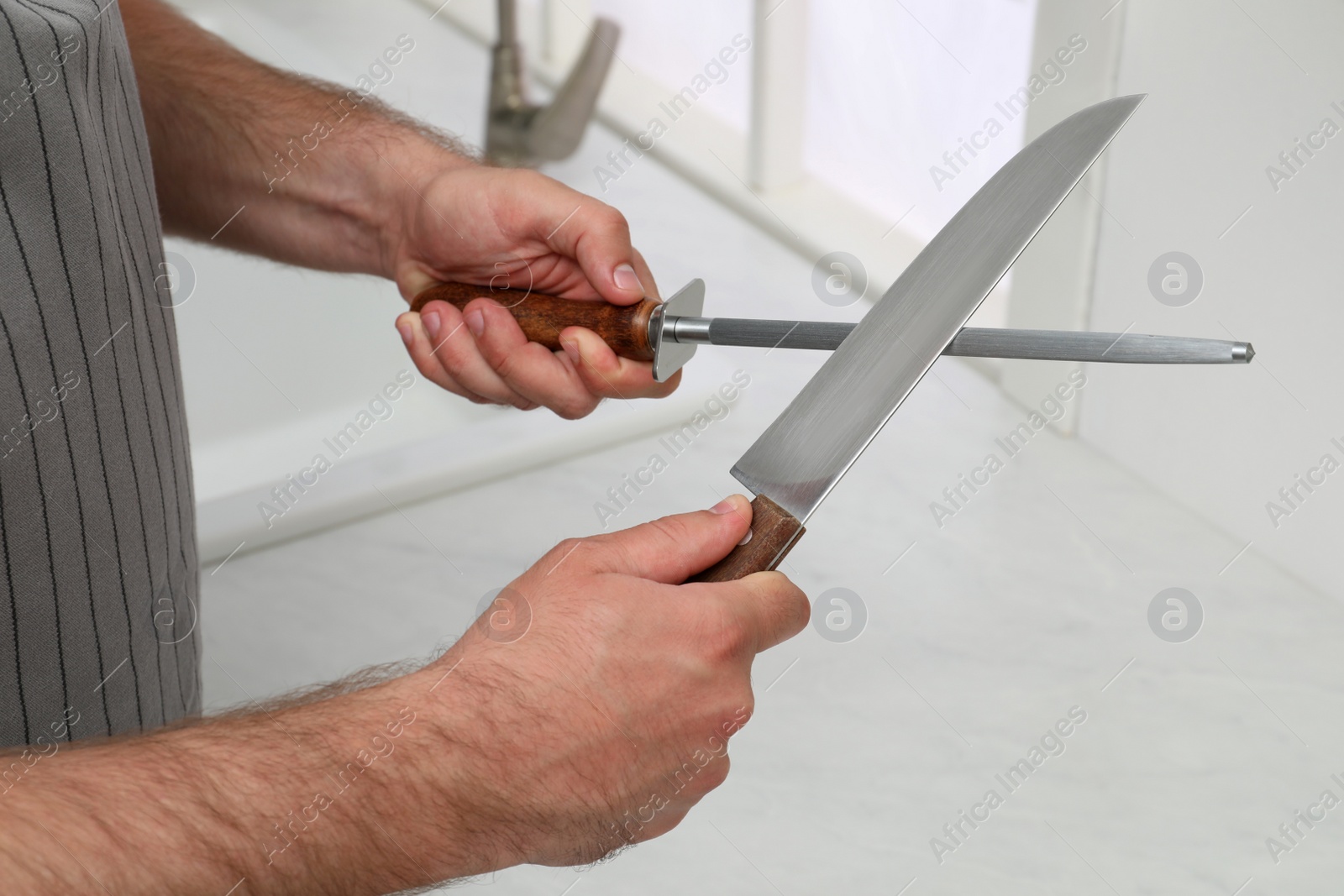 Photo of Man sharpening knife in kitchen, closeup view