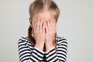 Girl covering face with hands on light grey background. Children's bullying