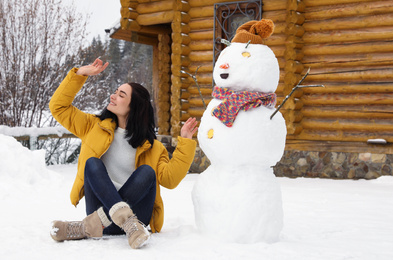 Photo of Young woman near funny snowman outdoors. Winter vacation