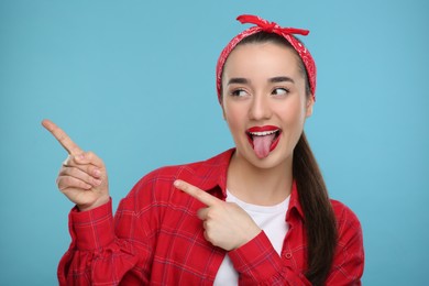Photo of Happy woman showing her tongue and pointing at something on light blue background