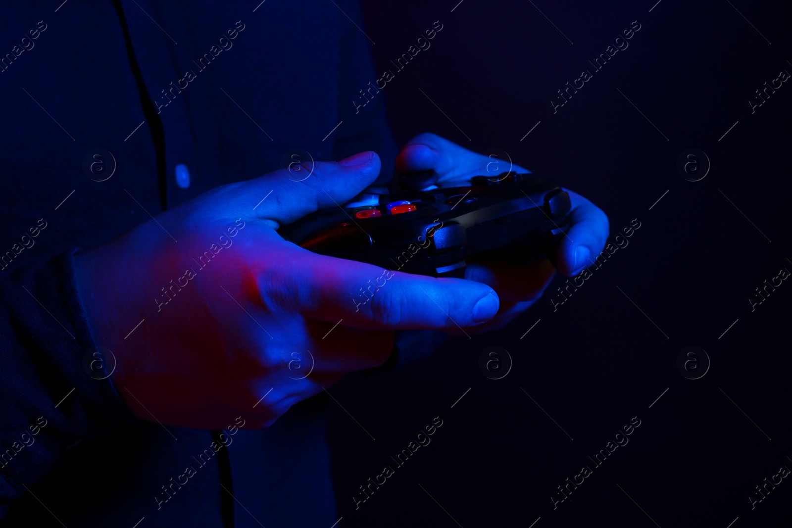 Photo of Man using wireless game controller on dark background in neon lights, closeup