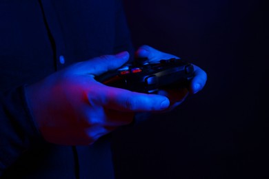 Photo of Man using wireless game controller on dark background in neon lights, closeup